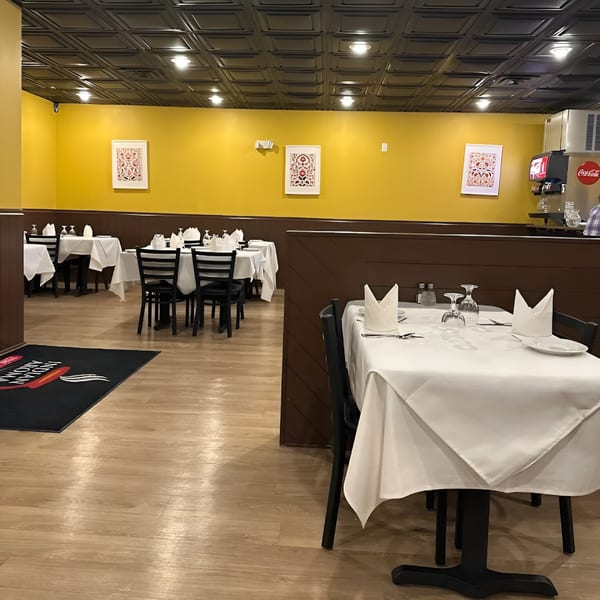 Interior of Indian Aroma restaurant with yellow walls, dark ceiling, set tables, and a soda fountain.