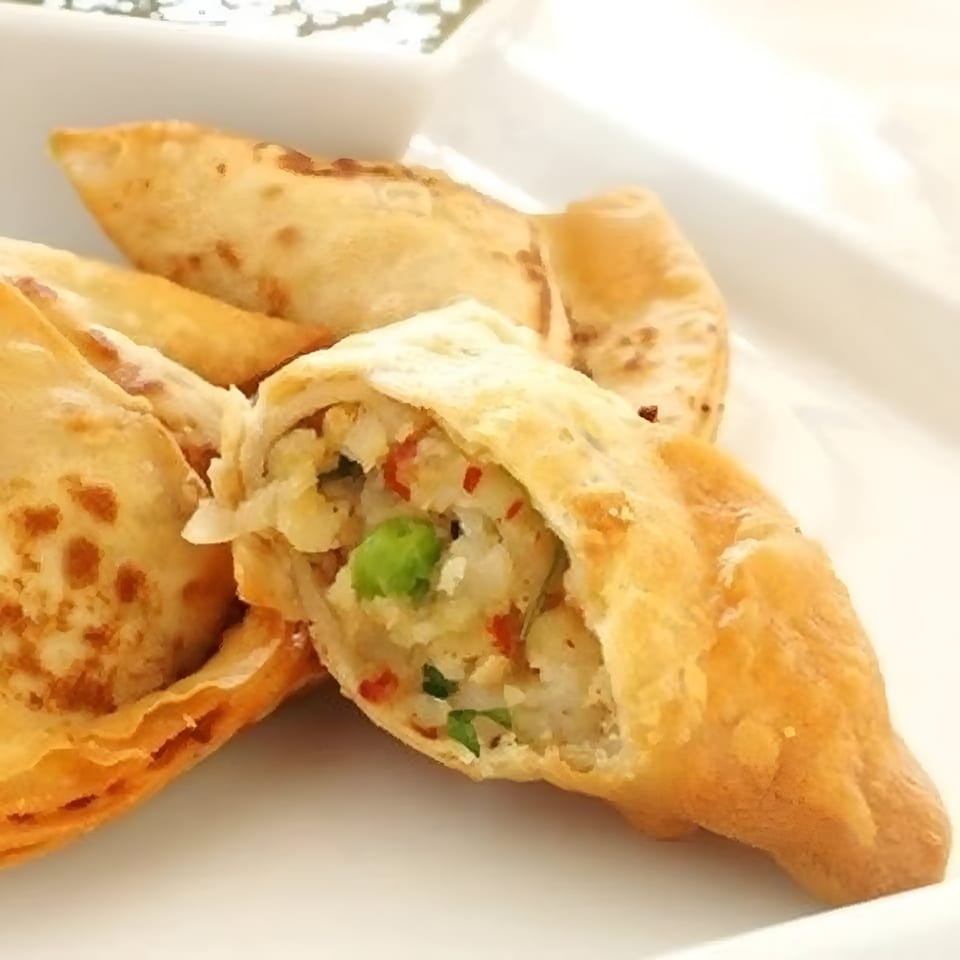 Close-up of golden-fried Indian samosas, one cut open to reveal a savory potato and pea filling.