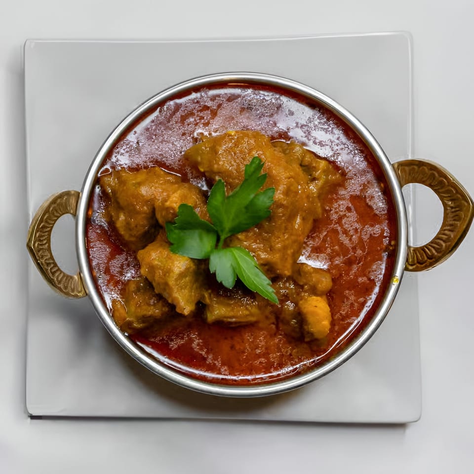 Indian Aroma's chicken curry in a metal bowl with ornate handles, garnished with parsley.
