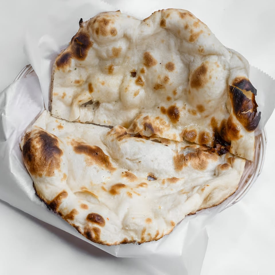 Two pieces of Indian naan bread, lightly charred, served in a white paper-lined basket.
