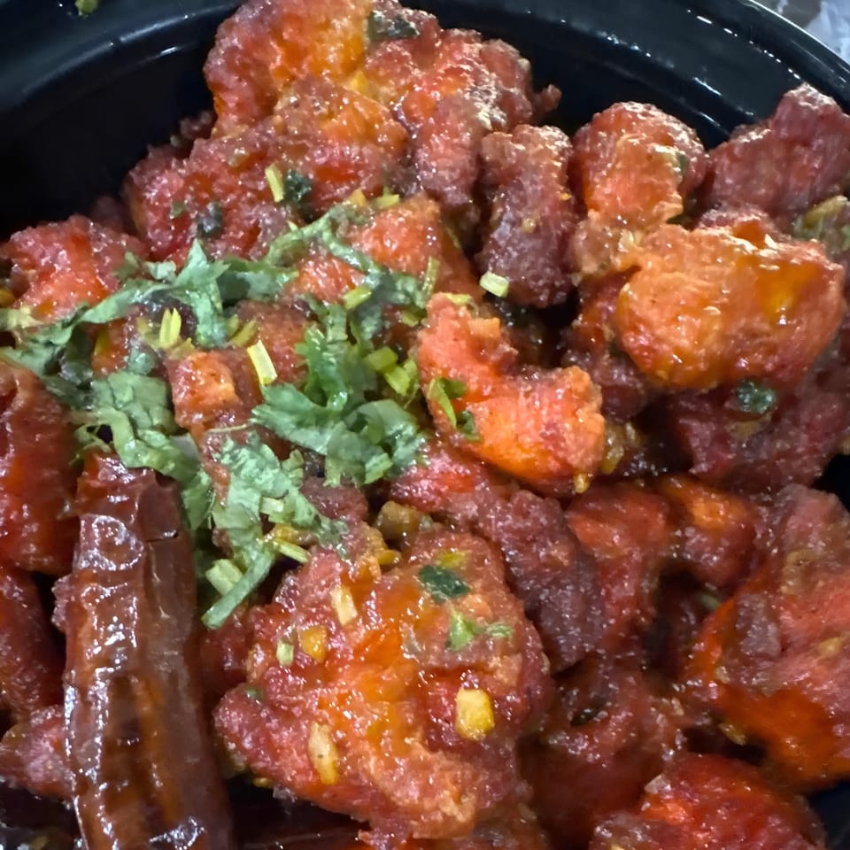 Close-up of Indian Aroma's chili chicken, garnished with fresh cilantro and dried red chilies.