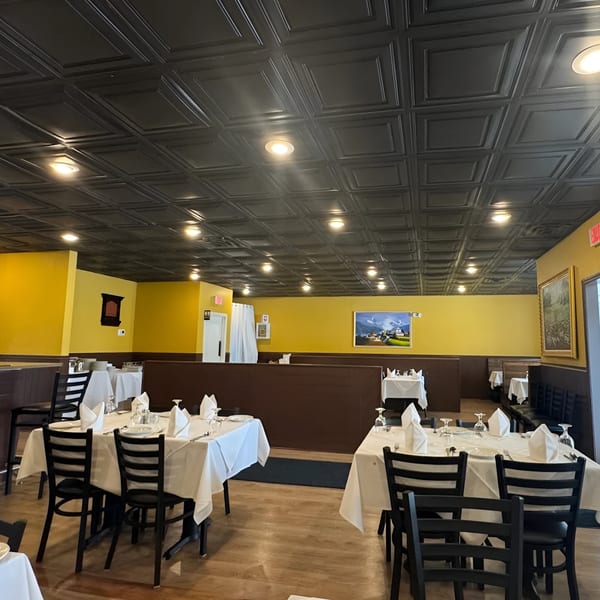 Interior of Indian Aroma restaurant with yellow walls, dark ceiling, and set tables with white tablecloths.