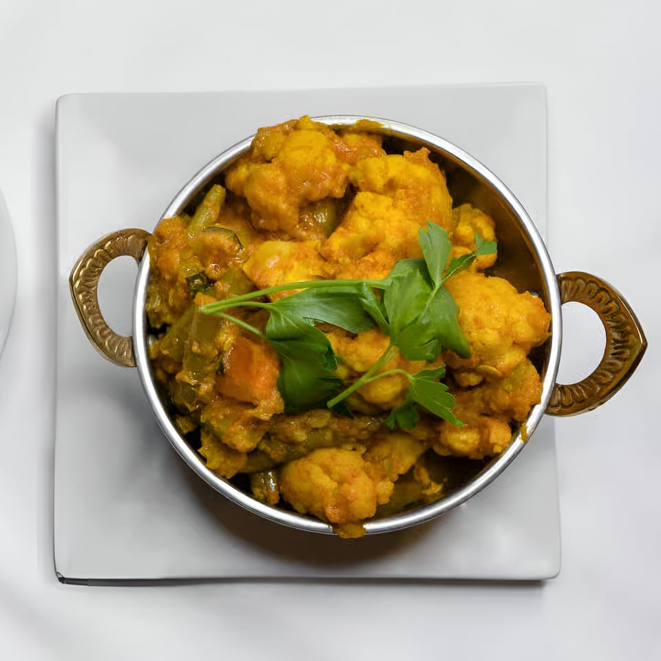 Indian Aroma's Gobi Manchurian, a vibrant cauliflower dish garnished with fresh parsley in a metal bowl.
