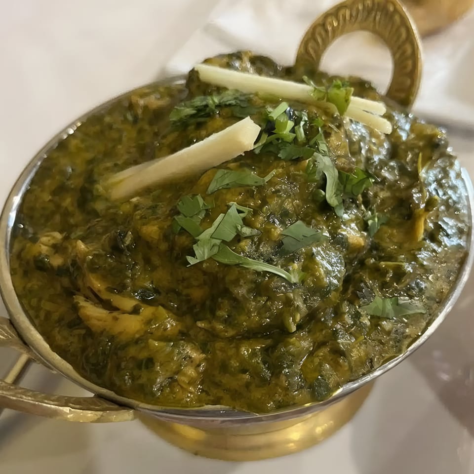 Indian Aroma's Palak Chicken, a vibrant green spinach and chicken curry, garnished with ginger and cilantro.