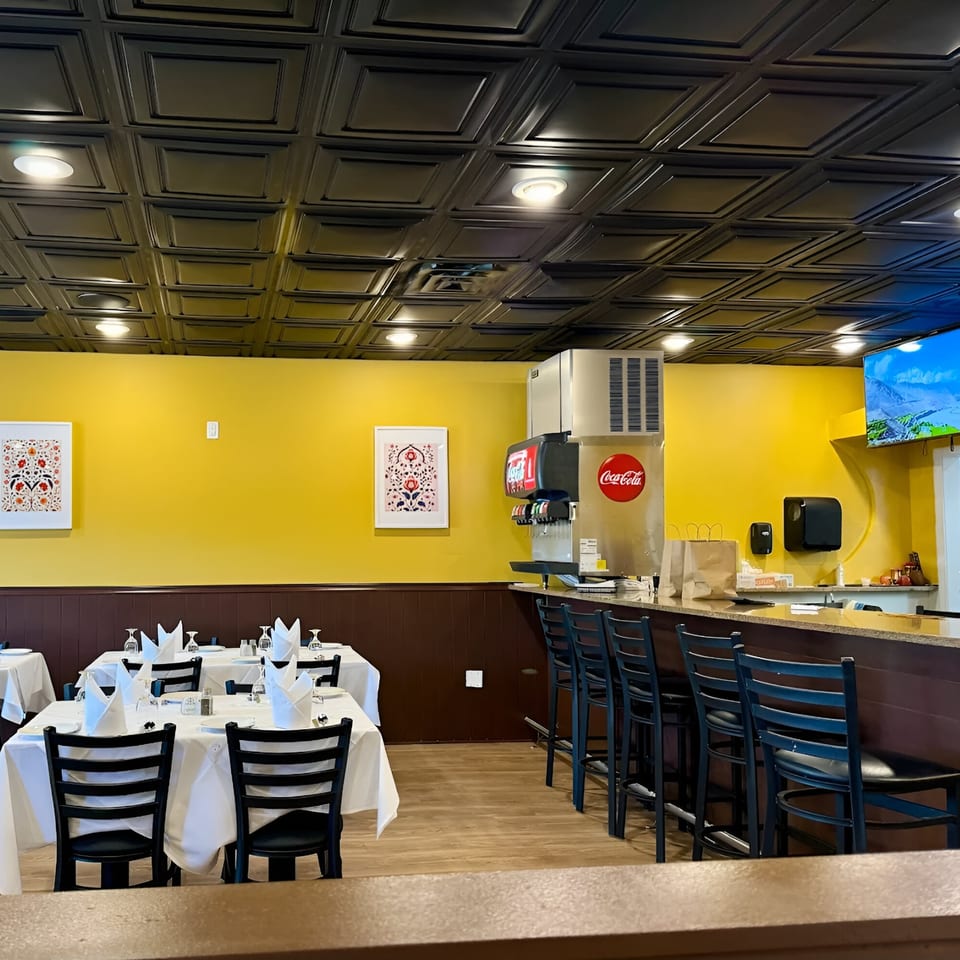 Interior of Indian Aroma restaurant with yellow walls, set tables, and a bar area with soda fountain.
